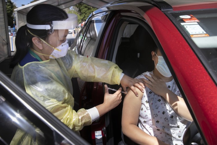 A health worker gives a COVID-19 booster shot on Tuesday at the Waipareira Trust drive-in COVID-19 testing station in Auckland, New Zealand. One factor that has driven case counts was the return of thousands of college students to the country last month.